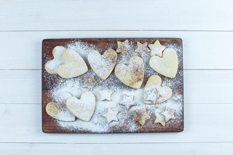 心形心形和星形饼干放在白色木板背景上的木质砧板上平铺明星美味桌子