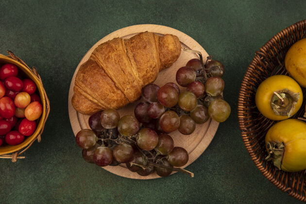葡萄栽培绿色表面上的木桶上放着牛角面包和柿子水果 厨房木板上放着甜葡萄的俯视图木桶葡萄厨房