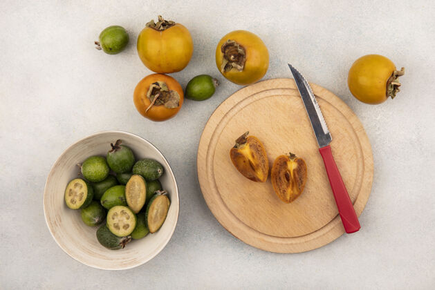 健康木制菜板上熟透的半个柿子果实的俯视图 菜板上有刀 碗上有飞珠 柿子被隔离在灰色的表面上秋天柿子甜点