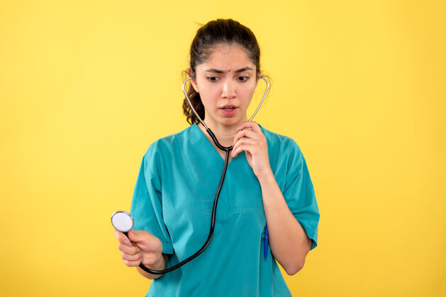 微笑前视图：穿着制服的女医生在黄色背景上使用听诊器人健康护士