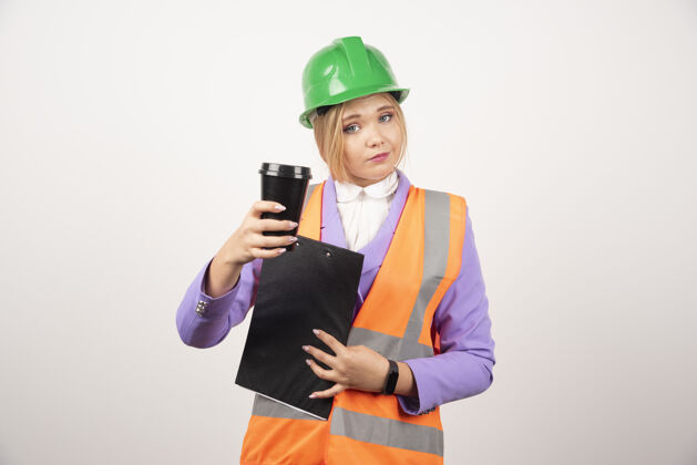 年轻人年轻的女工业工程师 穿着制服 白墙上挂着剪贴板和黑杯子工作女孩成人