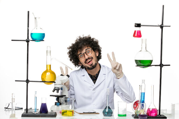 医院正面图身着医疗服的男性化学家坐在白色的办公桌上微笑着男化学家病毒前面