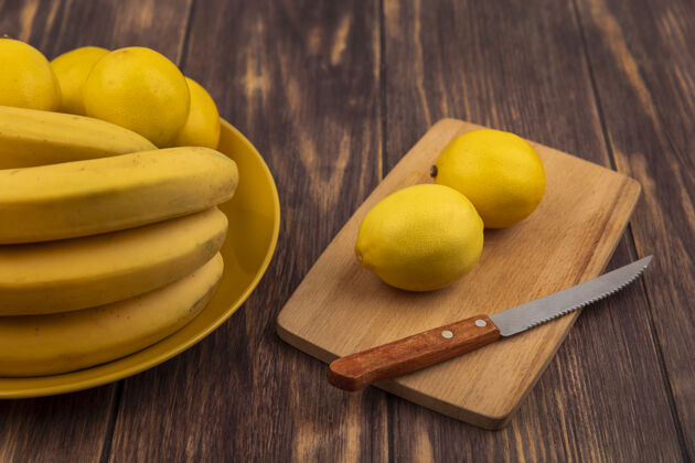 刀新鲜柠檬的顶视图在一个木制的厨房板与刀与柠檬在一个黄色的板与香蕉在木制表面健康柠檬板