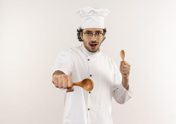 拿着快乐的年轻男厨师穿着厨师制服 戴着眼镜拿着勺子年轻眼镜男