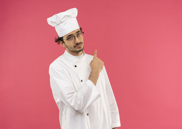 穿年轻的男厨师穿着厨师制服 戴着眼镜指着旁边年轻眼镜烹饪