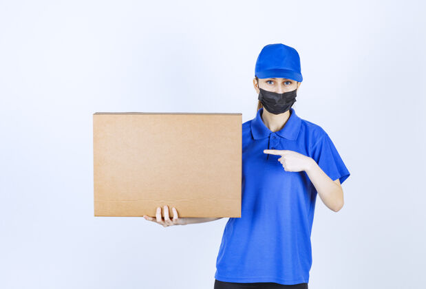 成人戴着面具和蓝色制服的女信使手里拿着一个大纸板包裹休闲外卖快速