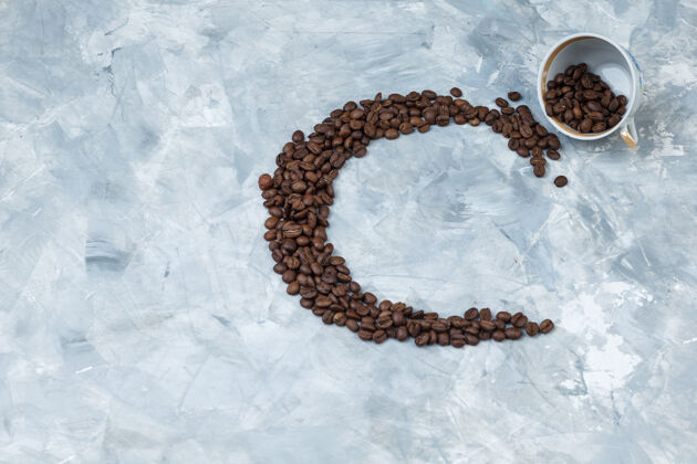 新鲜的咖啡豆在一个灰色灰泥背景上的白色杯子里顶视图农作物烤