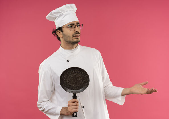 男性看着身边迷茫的年轻男厨师穿着厨师制服 戴着眼镜拿着煎锅 用手指着身边穿年轻持有
