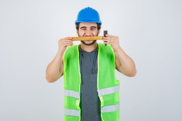 运动服年轻的建筑工人穿着制服 嘴上拿着锤子 看上去很可爱正视图建筑棕色头发锤子