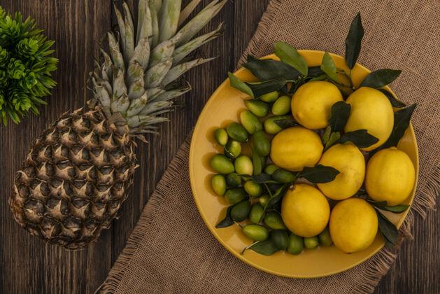 配料健康水果的俯视图 例如柠檬和金盏花 放在一个黄色的盘子里 放在一块布袋上 菠萝被隔离在一个木制的表面上柠檬水果木材