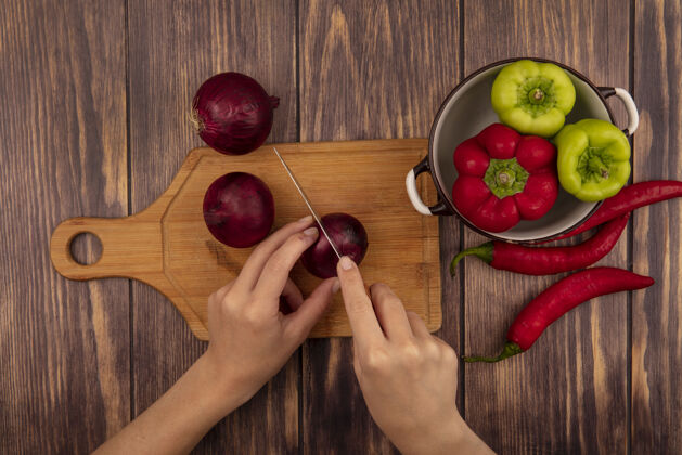 女性俯视图中的女性手切割一个木制菜板上的红洋葱与一个木制表面上的甜椒碗刀新鲜食物美食
