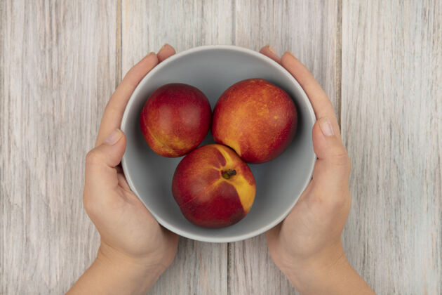 有机女性手拿着一碗新鲜甜桃子在灰色木头表面的俯视图饮食配料新鲜