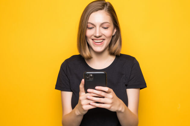 购物手拿智能手机 查看电子邮件 使用5g互联网 输入短信 站在黄色墙壁上的迷人女孩的肖像女性设备短信
