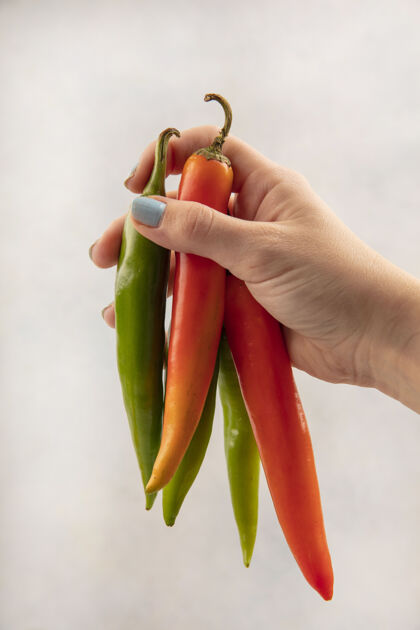 烹饪白色表面上手持橙色和绿色长辣椒的女性手的俯视图营养蔬菜膳食