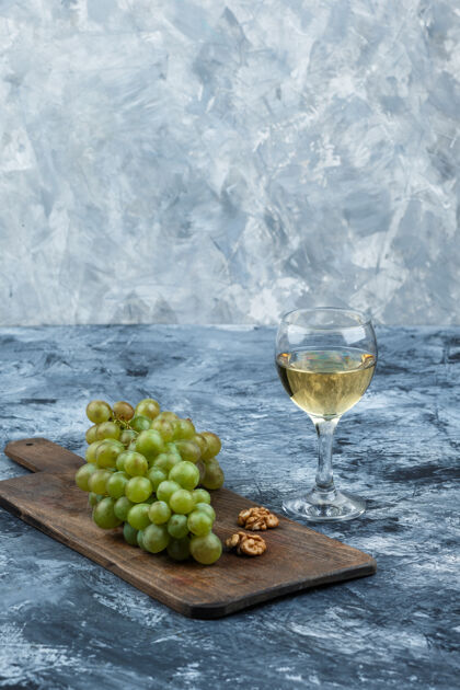 酒庄特写白葡萄 核桃放在砧板上 威士忌放在深蓝色和浅蓝色大理石背景上垂直自然浆果有机