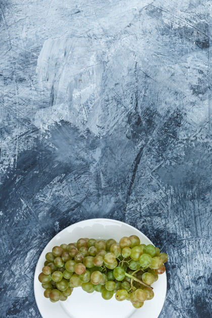 多汁绿色的葡萄放在一个白色的盘子里 背景是灰泥 平铺着成熟树枝食物