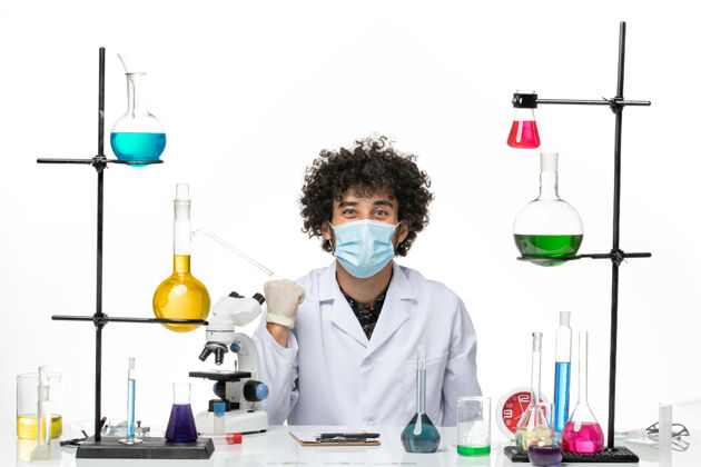 医生正面图：穿着白色医疗服 戴着面具的男性化学家坐在白色的空间里微笑着坐着化学面具