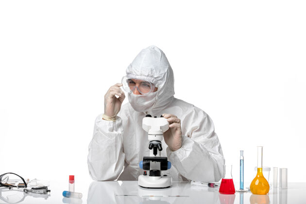 外套正面图男医生穿着防护服 戴着口罩 用显微镜观察白地板上大流行的健康病毒冠状病毒正面显微镜实验室