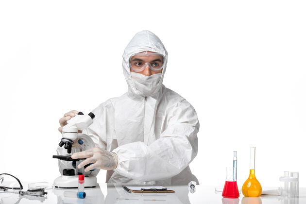 医学正面图：男医生穿着防护服 戴着面罩 在浅白的空间里使用显微镜显微镜防护大流行