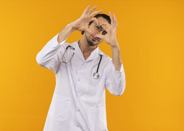 长袍年轻医生戴着医用眼镜 穿着医用长袍 听诊器显示心脏姿势医学黄色手势