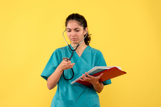 护士前视图困惑的女医生穿着制服拿着黄色背景纸用听诊器医学手持听诊器