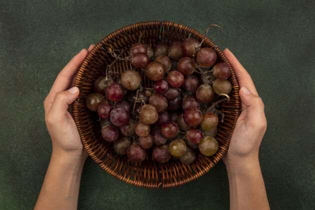自然顶视图中的女性手拿着一桶新鲜健康的葡萄在绿色的表面桶农场美味