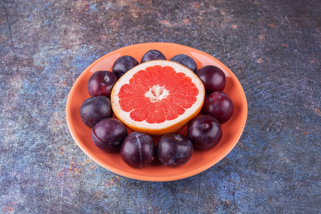 生的把一片葡萄柚和美味的李子放在一个橙色的盘子里美味李子一半