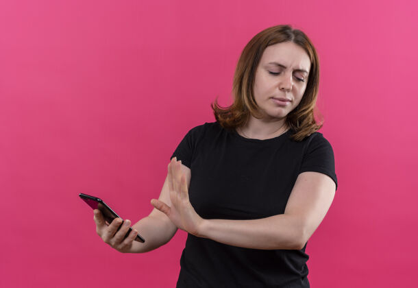 抱着一个年轻随意的女人拿着手机 在孤零零的粉色墙上做着“不”的手势年轻不愉快女孩