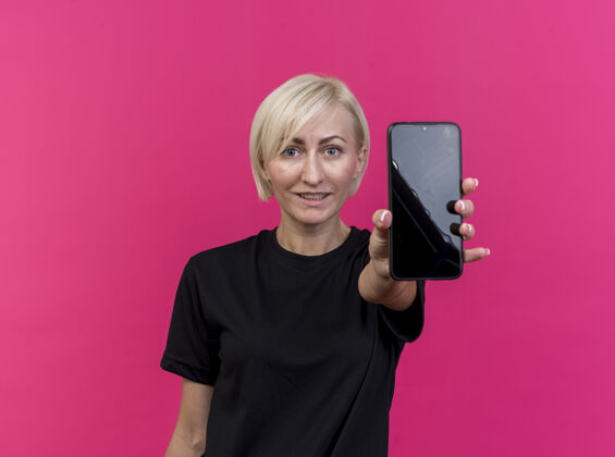 电话高兴的中年金发斯拉夫女人伸出手机对着隔离在深红色墙上的复制空间中年手机金发