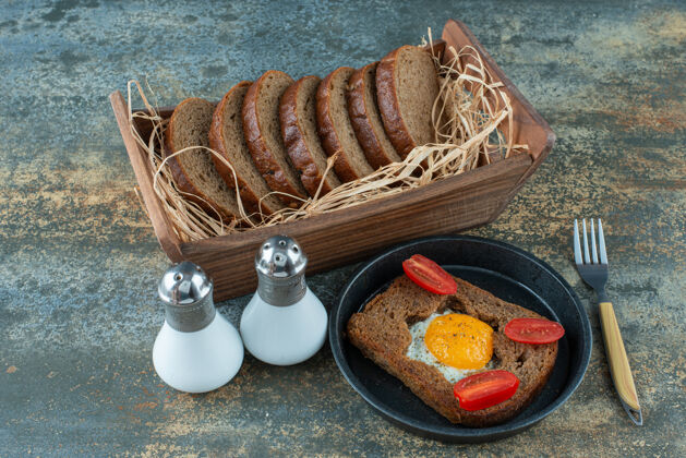 西红柿一个黑色的平底锅 大理石背景上有煎蛋和棕色面包片面包美味一餐