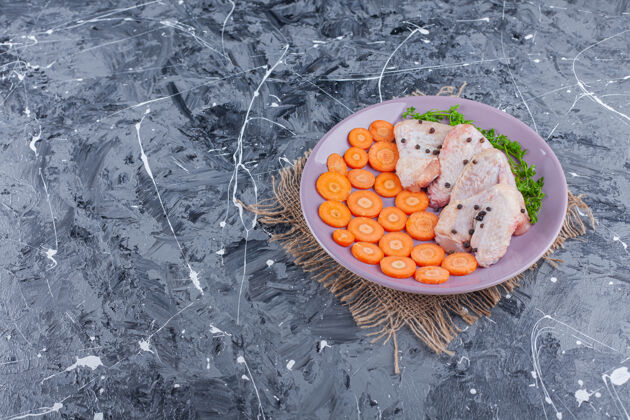 新鲜把胡萝卜片 鸡翅和青菜放在盘子里的粗麻布上 放在蓝色的上面生的美味生的