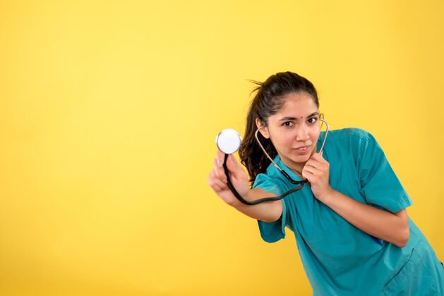 人站在黄色墙上的年轻女医生手持听诊器的正面图年轻女医生抱人