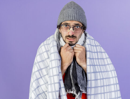 男人焦急的年轻白种人 戴着眼镜 戴着冬天的帽子 围着格子呢围巾 手放在胸前 隔离在紫色的墙上 留着复印空间包裹格子布围巾