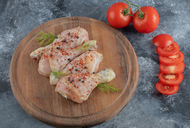 烹饪生鸡腿加香料和切成片或整片的西红柿放在木板上烧烤木板厨房