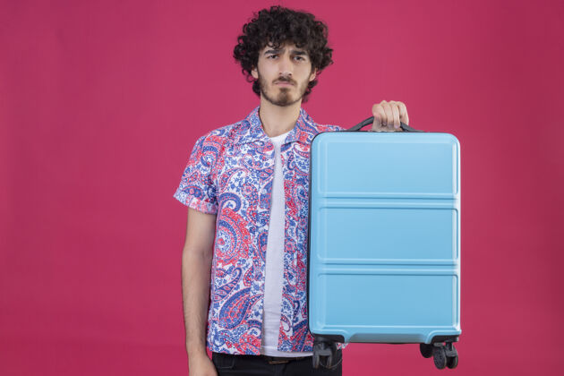 抱着年轻英俊 卷曲的旅行家 拿着手提箱 站在一堵粉红色的墙上 留着复印空间男人手提箱讨厌