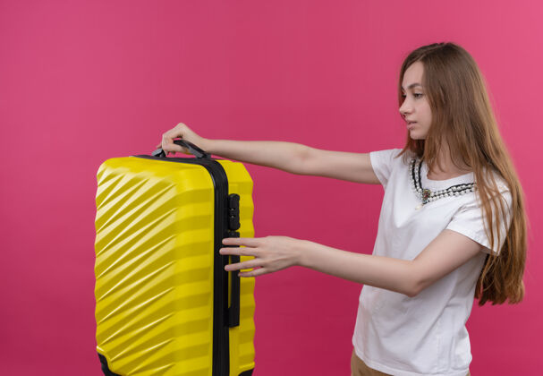站立年轻的旅行女孩拿着手提箱站在孤立的粉红色墙上的侧视图上女孩年轻手提箱