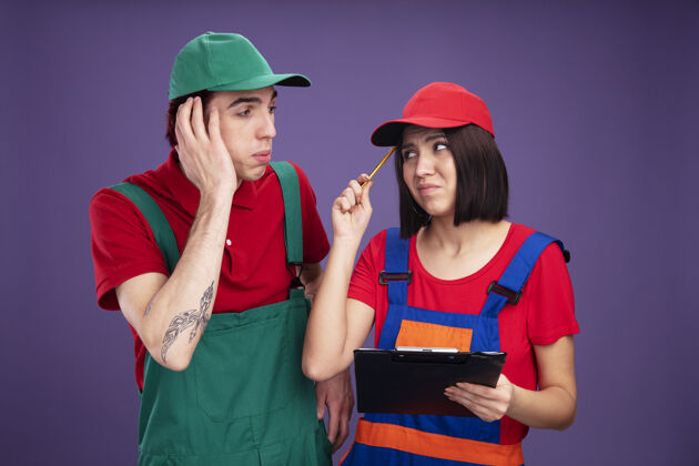 工人一对穿着建筑工人制服 戴着帽子的年轻夫妇看着对方不高兴的女孩拿着铅笔和剪贴板用铅笔碰头关心的家伙手放在头上每一个持有保持