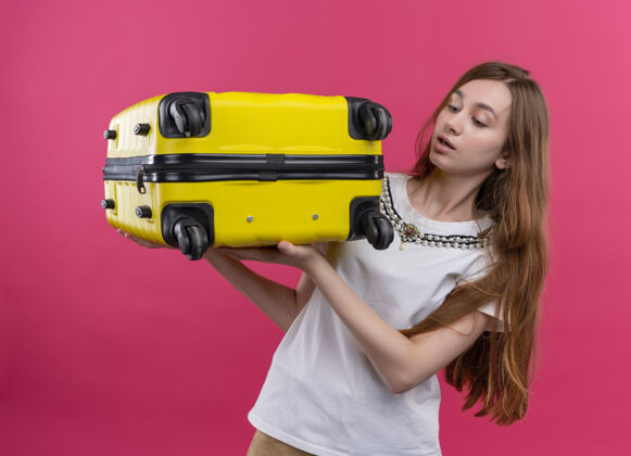 女孩一个年轻的旅行家女孩把手提箱放在孤零零的粉红色墙上年轻人拿着手提箱
