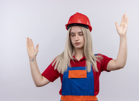 年轻一个年轻的金发女孩 穿着制服 双手举着 眼睛闭着 站在隔离的白墙上女孩制服工程师