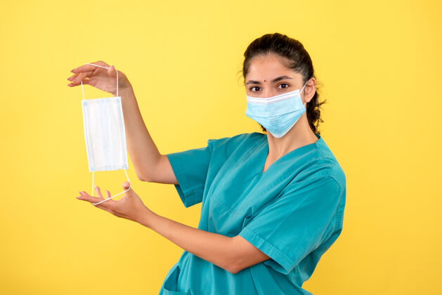 手黄墙上戴着口罩的女医生手拿口罩的正视图前面欢呼脸