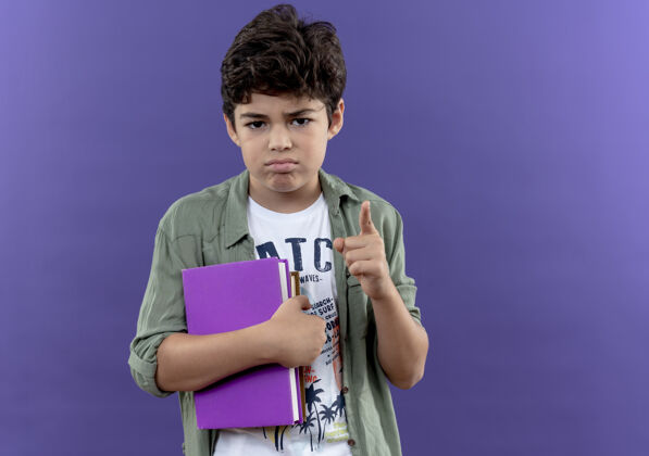拥抱悲伤的小男生拿着书 用“是”的手势孤立地站在紫色的墙上手势小男孩表演