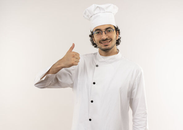 穿着面带微笑的年轻男厨师穿着厨师制服 戴着眼镜 他的大拇指孤立地竖在白色的墙上微笑年轻大拇指