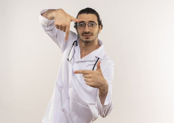 听诊器年轻的男医生戴着眼镜 穿着白色长袍 听诊器 在隔离的白色墙壁上显示出拍照的姿势 并留有复印空间请医生光学