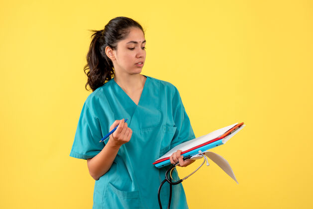 年轻女医生身着制服的年轻女医生站在黄色墙壁上检查文件的正面图护士检查纸