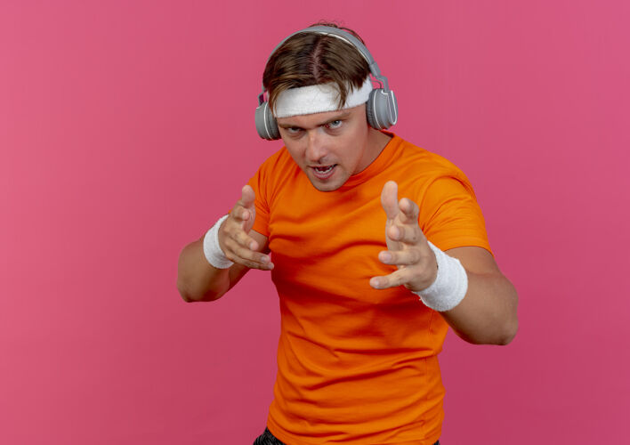 空间自信的年轻帅气的运动型男人戴着头带和腕带 戴着耳机 伸出双手隔离在粉色的复制空间里复制手运动