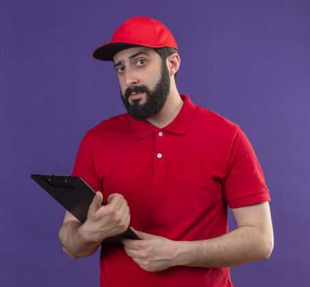 紫自信年轻英俊的白人送货员身穿红色制服 戴着紫色帽子剪贴板年轻自信