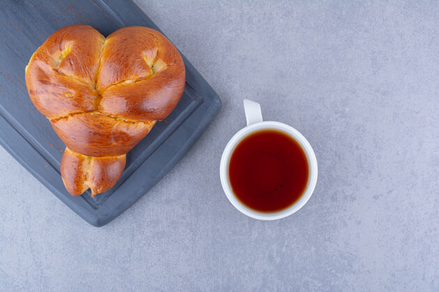 板一杯茶和一个心形的甜面包放在大理石表面的海军蓝板上风味小吃糕点