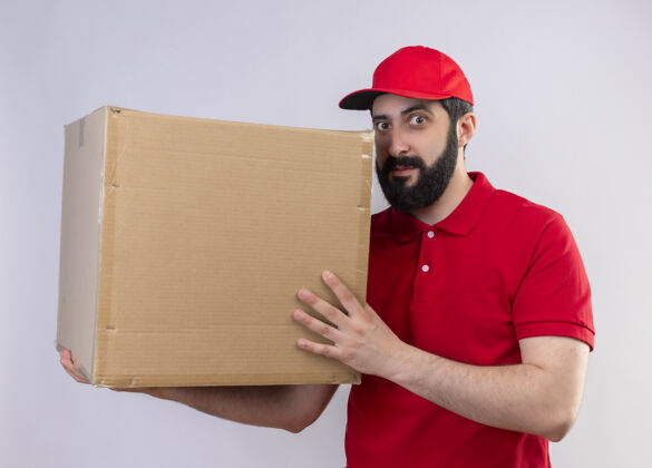 交货印象深刻的年轻英俊的白人送货员穿着红色制服 戴着帽子拿着纸箱 抬头望着孤立的白色制服男人帅气