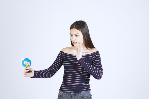 旅行穿着条纹衬衫的年轻女子拿着一个迷你地球仪 想阻止它成人女性人类