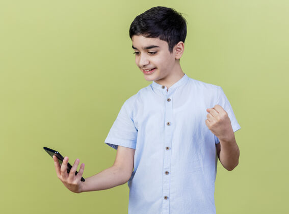 电话在橄榄绿的背景下 微笑着的白人小男孩抱着手机 看着手机做着“是”的手势手势年轻奥利弗